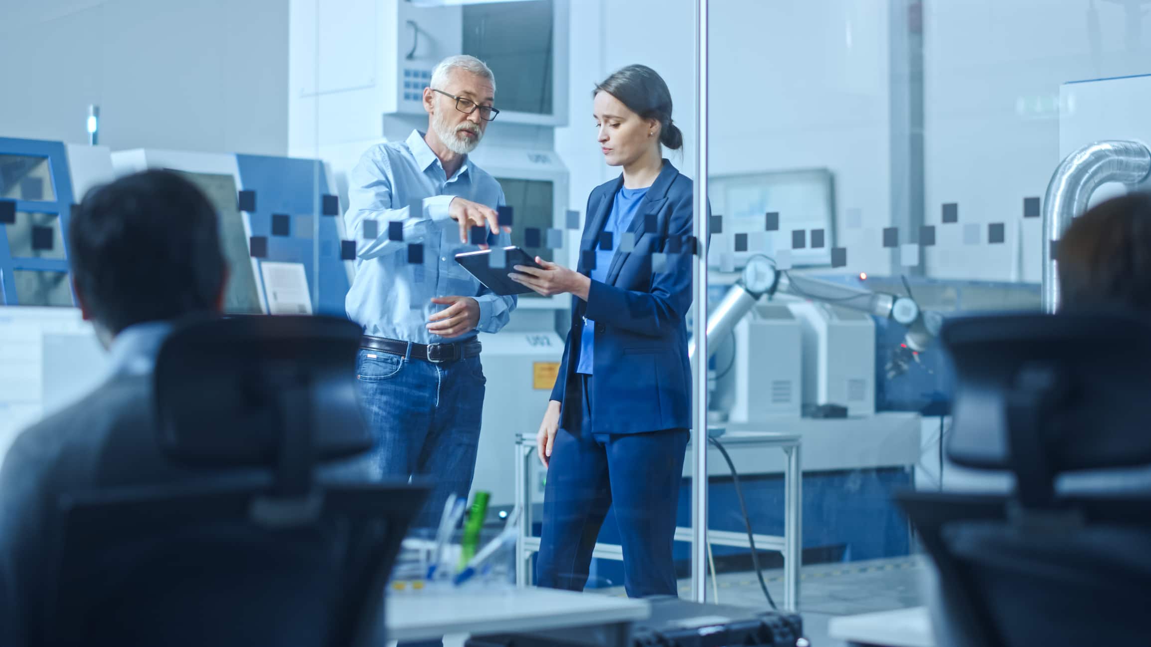 Un interim manager experimentado y una ejecutiva revisan datos empresariales juntos en un entorno de alta tecnología, representando la elección correcta de liderazgo temporal.